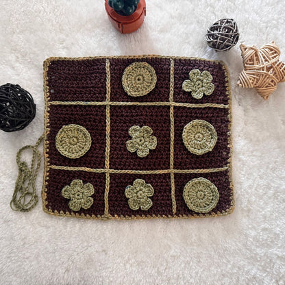 Crocheted tic-tac-toe board with flower patterns on a textured surface.