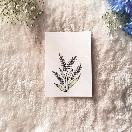 Light purple colored petals on stalks with green leaves painted on a white card placed on a textures surfaces with decorative flowers in the background 