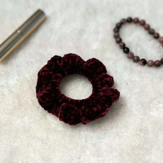 maroon velvet crochet scrunchie place on soft cloth with a lipstick and a bracelet in the background  
