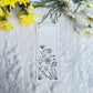Floral sketch in black and white on a bookmark placed on fur fabric with fresh flowers in the background 