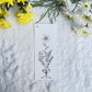 Single flower stalk bouquet sketch in black and white on a bookmark placed on fur fabric with fresh flowers in the background 