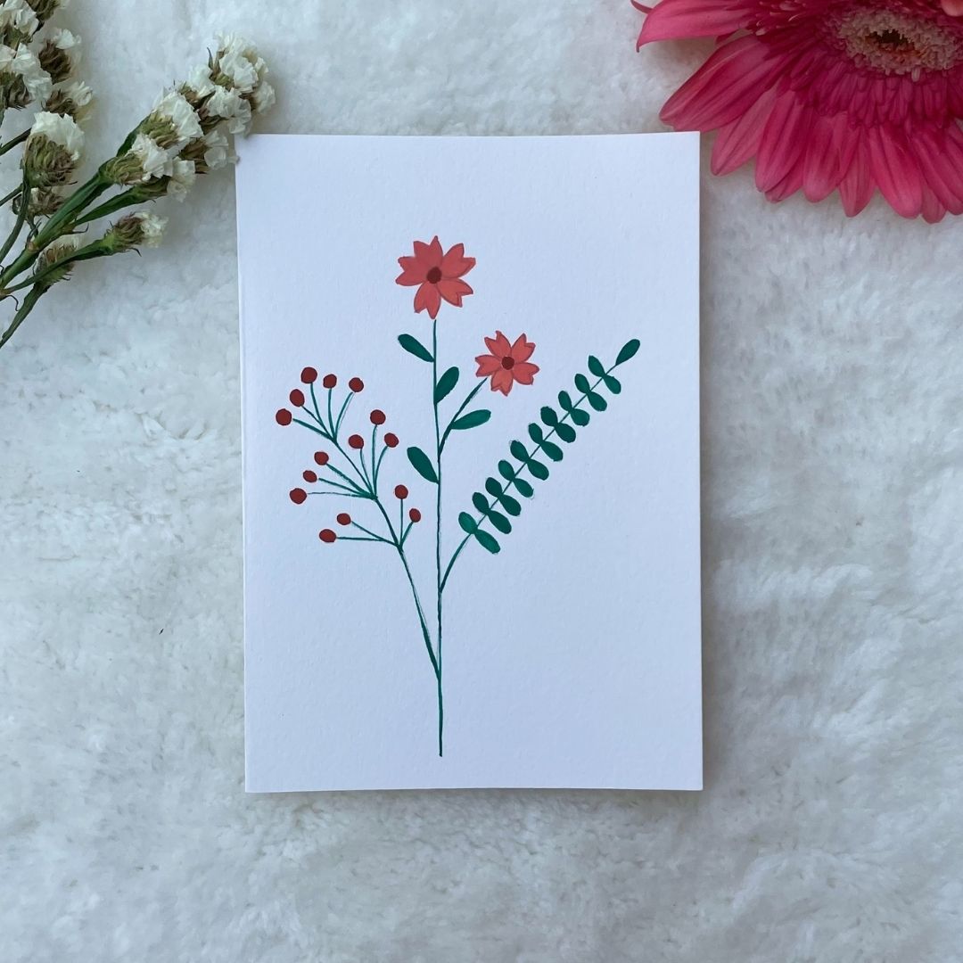 A hand-painted greeting card with peach floral minimalist bouquet on a white background, displayed on a fluffy surface with a small branch of leaves to the side.