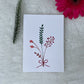 A hand-painted greeting card with a peach minimalist bouquet gouache illustration of small leaves on a white background, displayed on a fluffy surface with a small branch of leaves to the side.