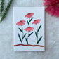 A hand painted floral themed card with pink flowers on white card stock placed on a fur cloth with flowers and leaves in the background 