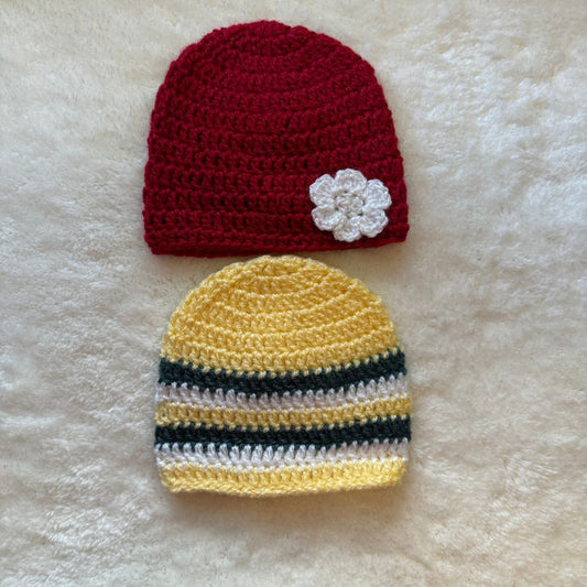 Two crochet baby beanies, one in red with a white flower on the front and the other in yellow with grey and white stripes placed on a a white fur cloth 