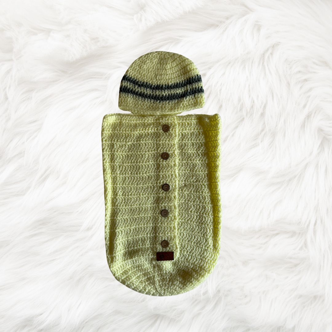 Yellow button down Crochet baby cocoon with a baby beanie placed on a white fur fabric
