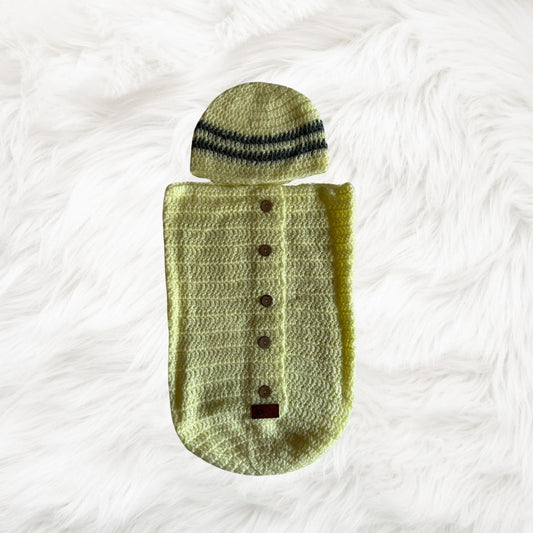 Yellow button down Crochet baby cocoon with a baby beanie placed on a white fur fabric